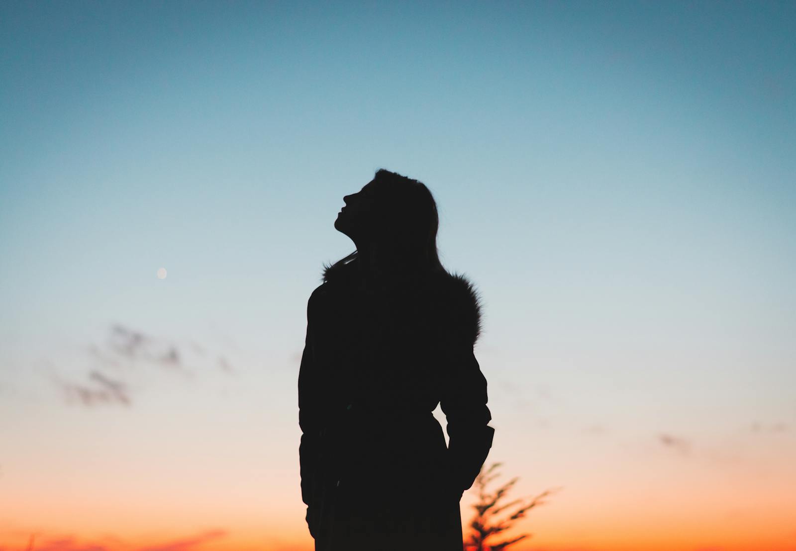 A woman silhouetted against a vibrant sunset sky, evoking peace and contemplation.